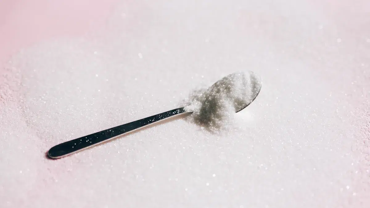 A silver spoon nestled in a mound of white sugar on a pink background.