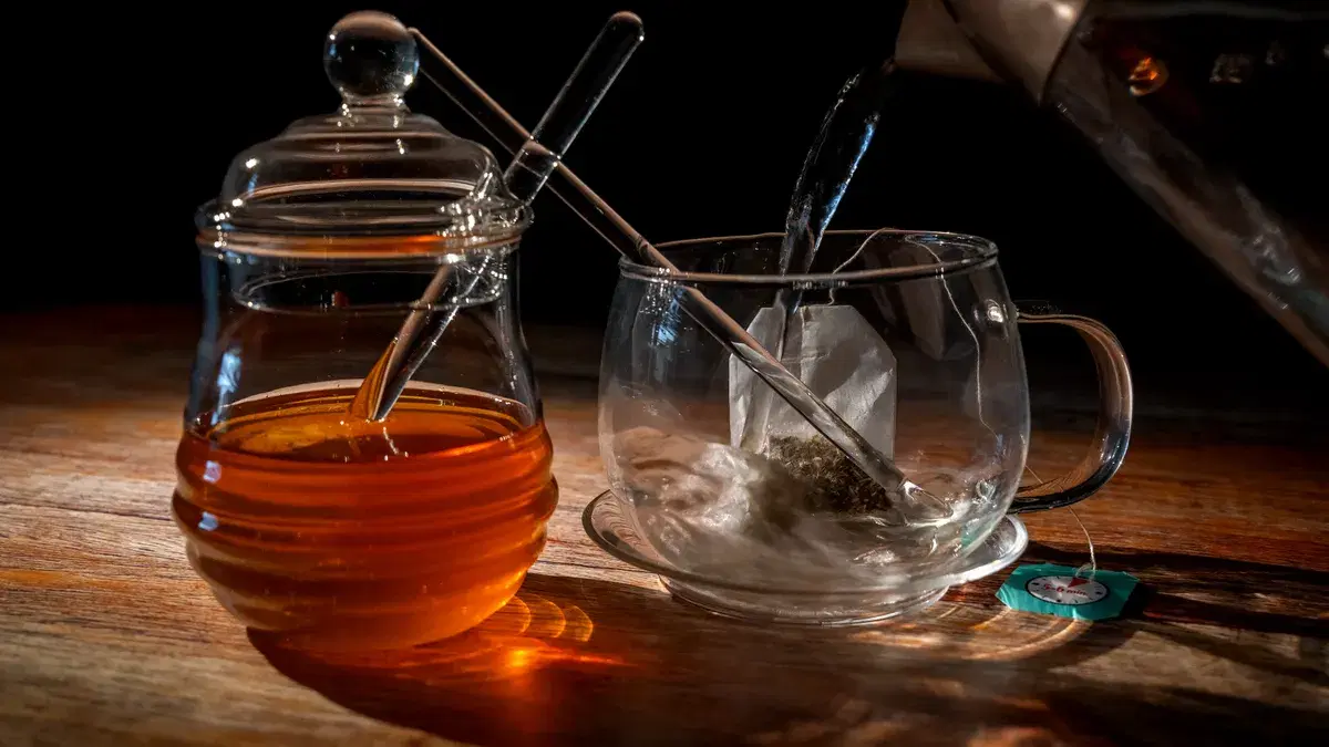 A glass teacup and honey jar on wooden table, capturing the steam and warmth of freshly brewed tea.