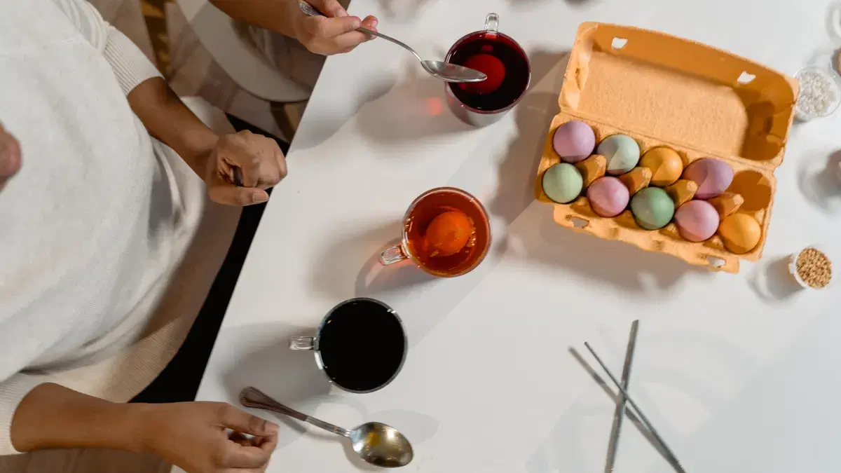 Top view of people coloring Easter eggs with various dyes on a table.